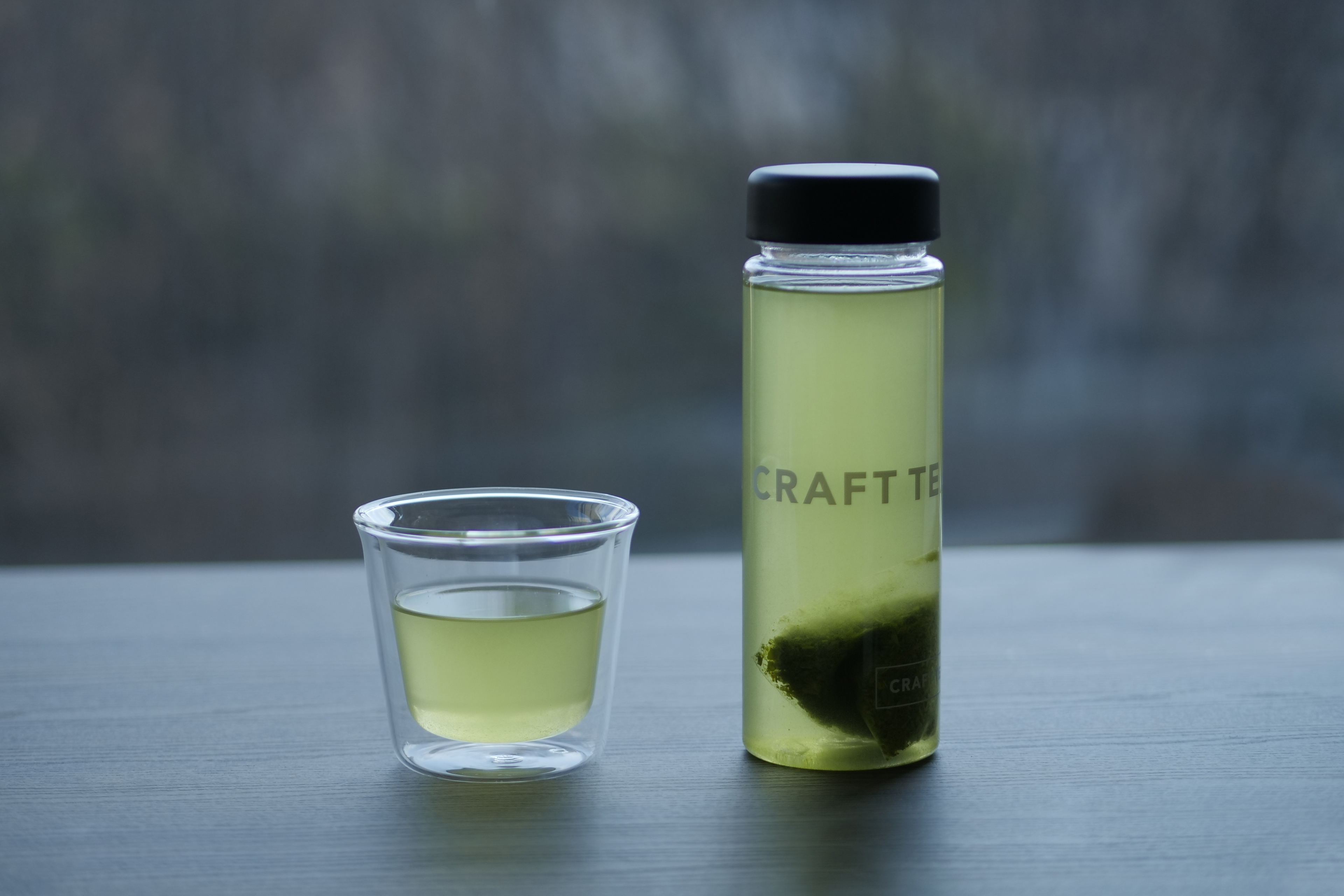 窓辺に置かれたCRAFT TEAボトルと二重グラス